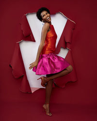 The side of a model wearing an orange and magenta silk satin dress in a red room