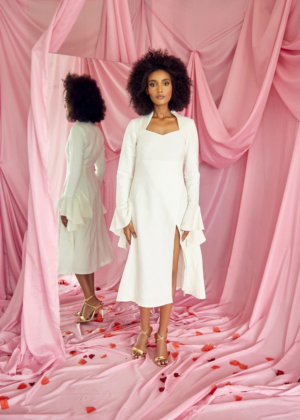 A model wearing a white linen dress with a side slit in a pink setting