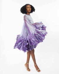 The side of a model wearing a Purple asymetric sleeve mini dress with ruffles and silk slip lining