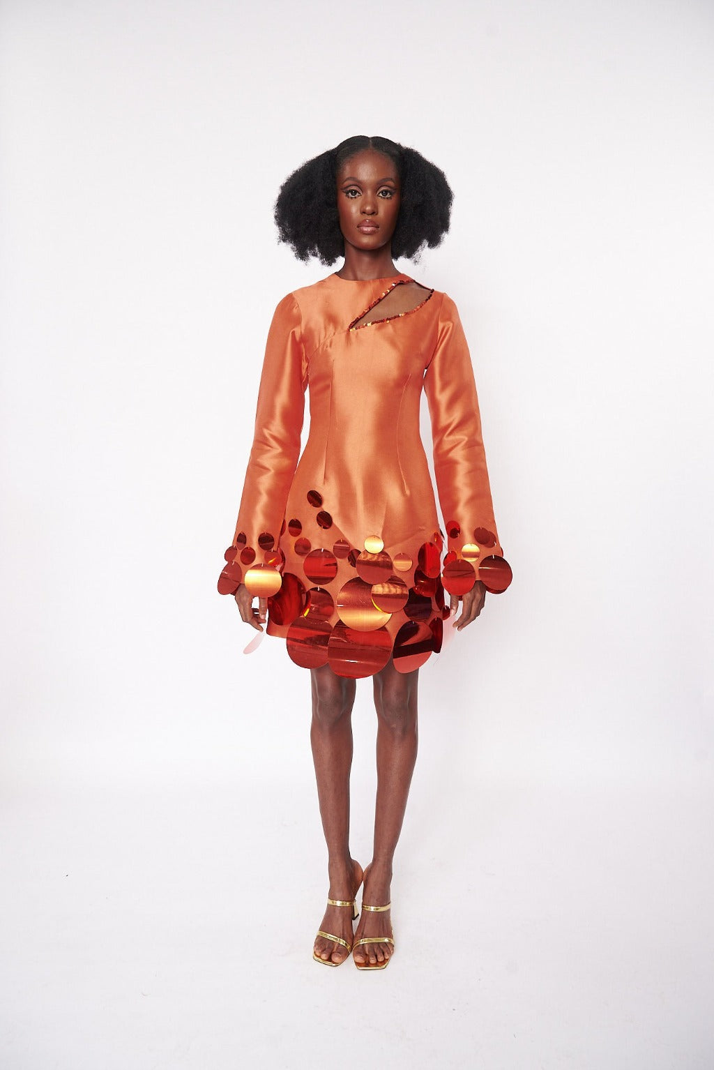 A model wearing an Orange mini dress with side cut-out detail at the neckline and embellished with sequins at the hem and sleeves