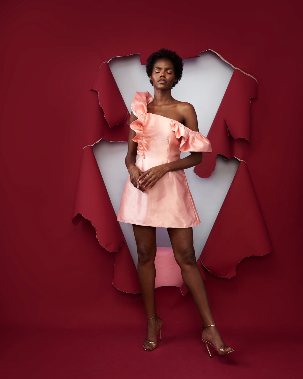 A model wearing a peach colored dress in a red room