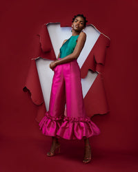 A model posing wearing a green silk satin top and magenta silk satin pants with ruffle hem culottes in a red room