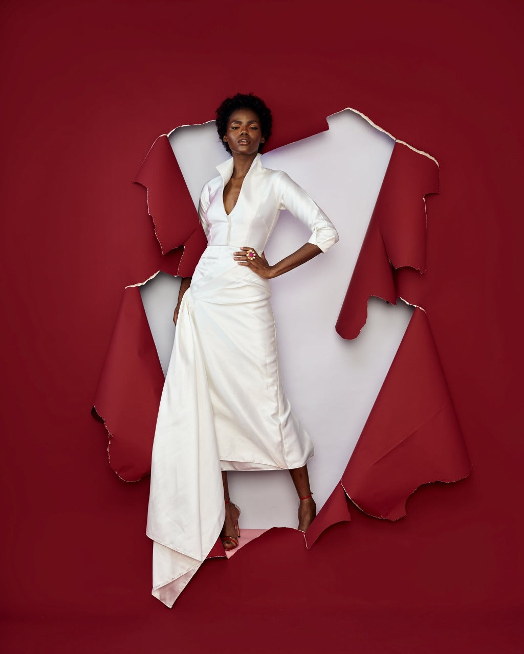 A model posing in a red room while wearing a white silk satin dress