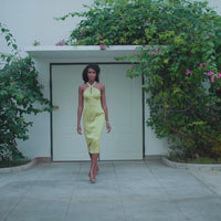 A model wearing an olive halter neck dress in front of a house