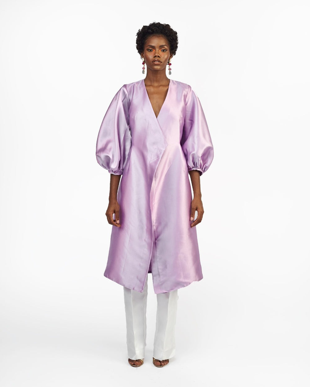 A model in a Lilac silk satin jacket with puff sleeve and a White straight-cut pant in a white room