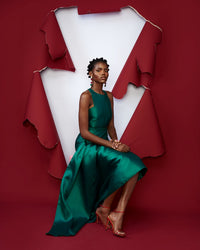 A model sitting down wearing a green silk satin top and skirt in a red room