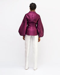 The back of a model wearing aubergine colored silk satin jacket with white pants