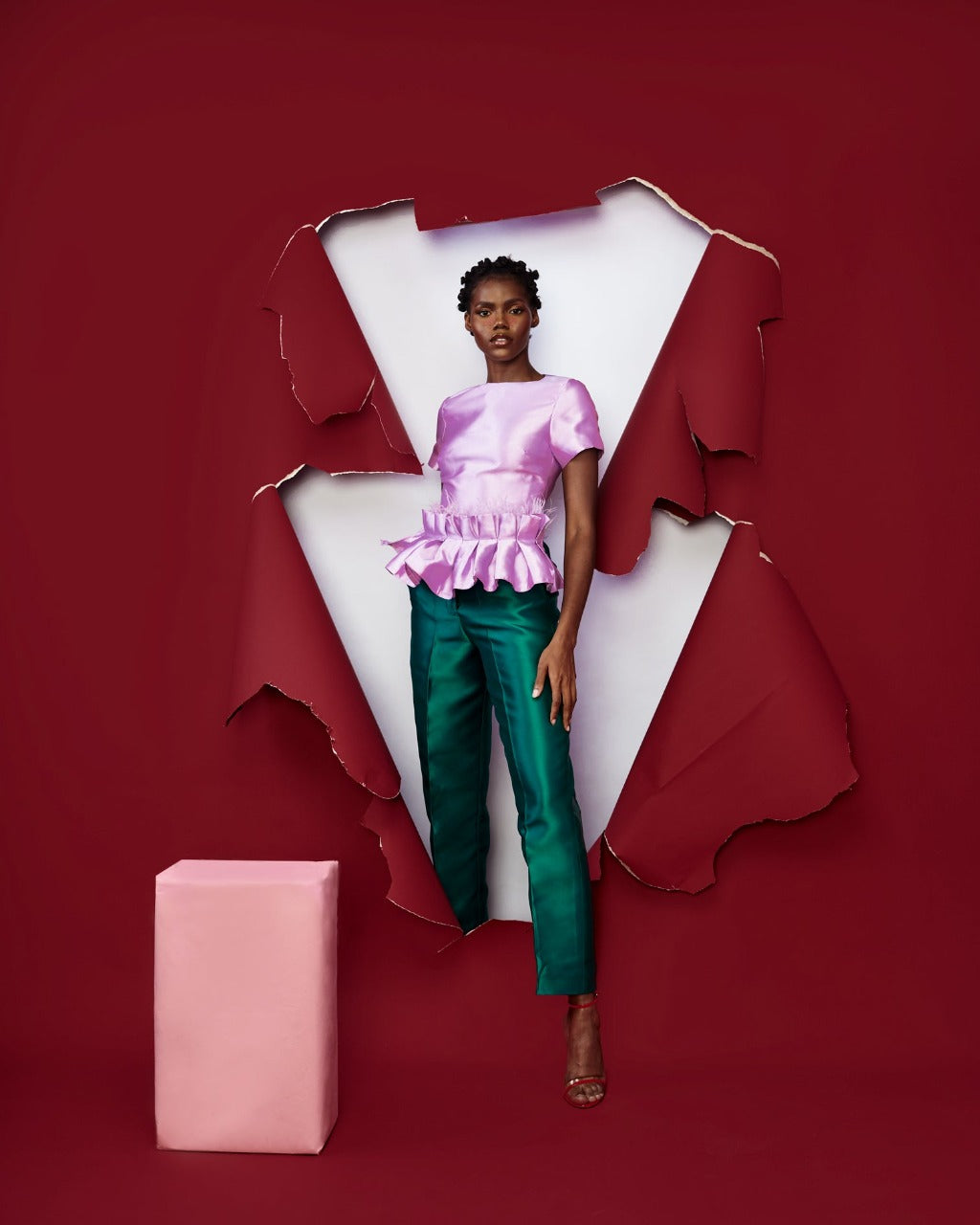 A model posing in a red room while wearing green silk satin pants with a purple satin top