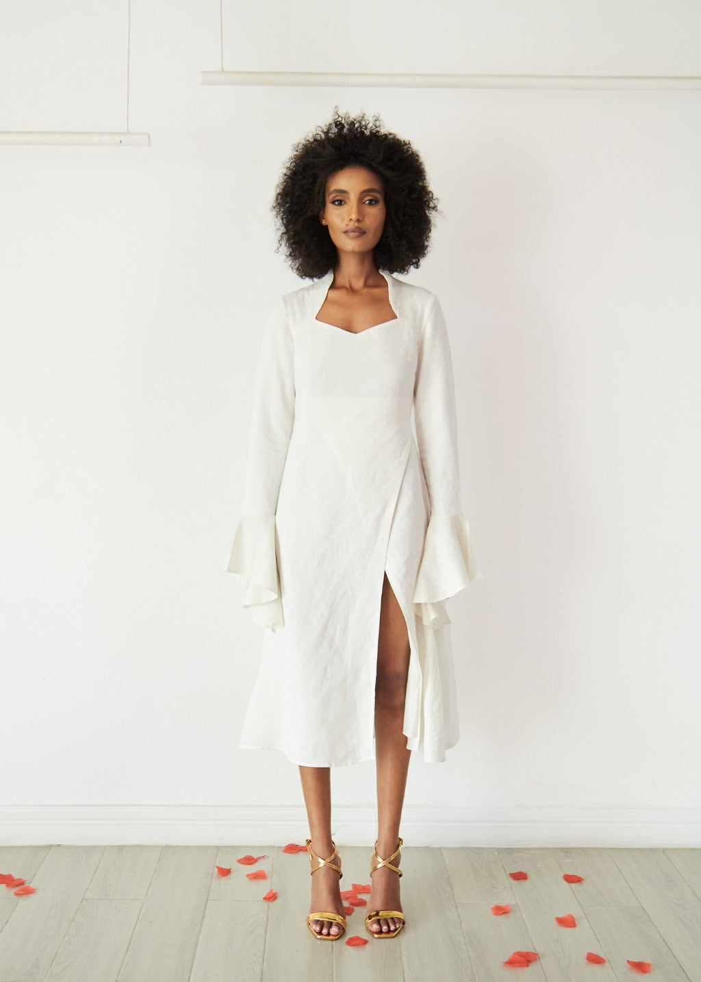 A model wearing a white linen dress with a side slit in a white room