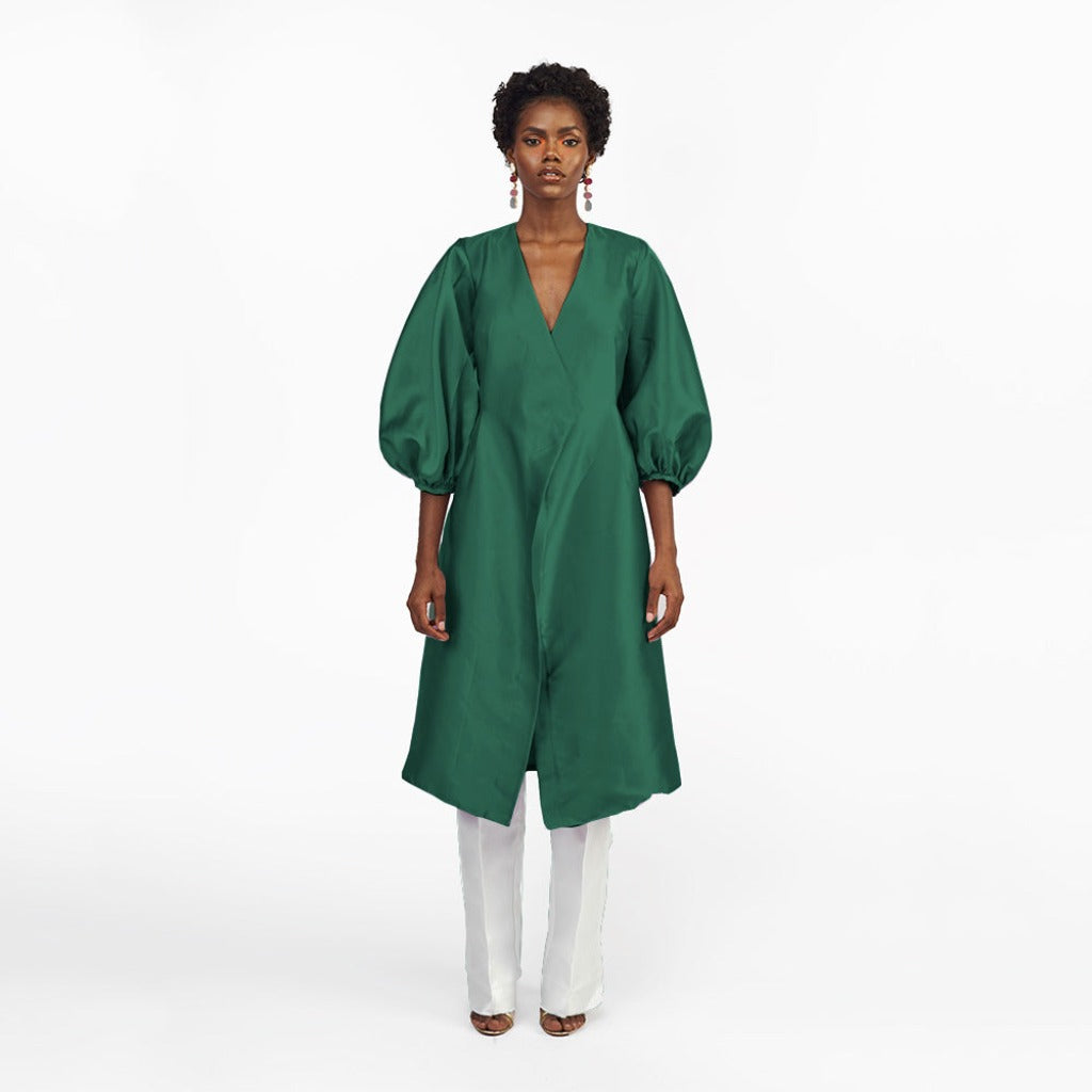 A model in a green silk satin jacket with puff sleeve and a White straight-cut pant in a white room