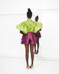 the back of a model wearing a lime green top and Aubergine colored shorts with ruffles in a white room