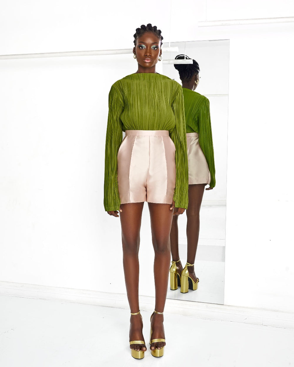A model wearing an Olive top and Nude colored shorts in a white room
