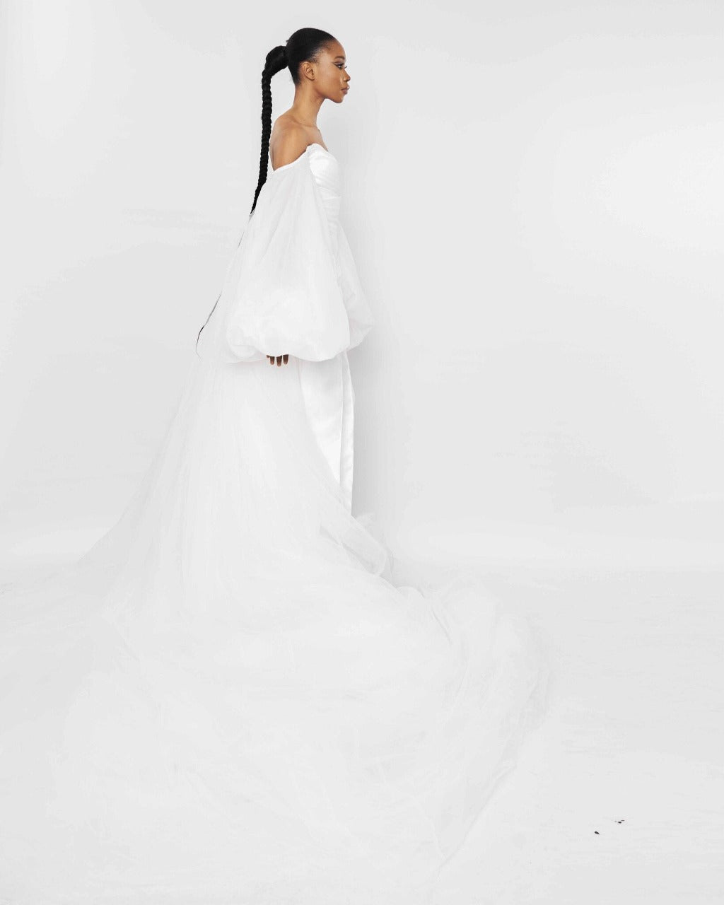 The side of a model wearing an off-shoulder White jumpsuit with exaggerated sleeves and tulle flare