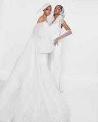 Two models wearing an off-shoulder White jumpsuit with exaggerated sleeves and tulle flare