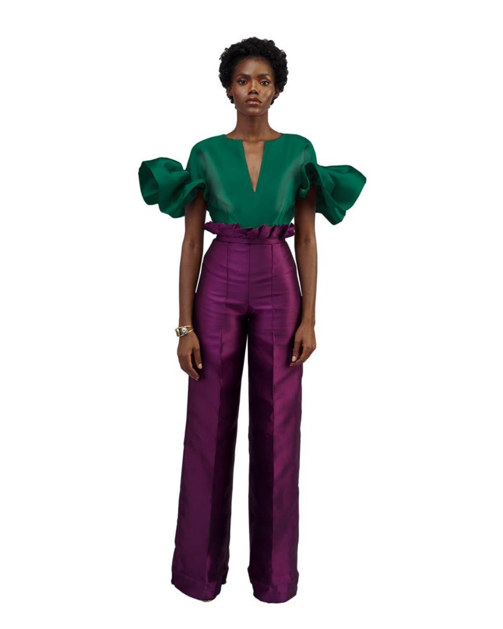A model wearing aubergine colored pants with a green top in a white room