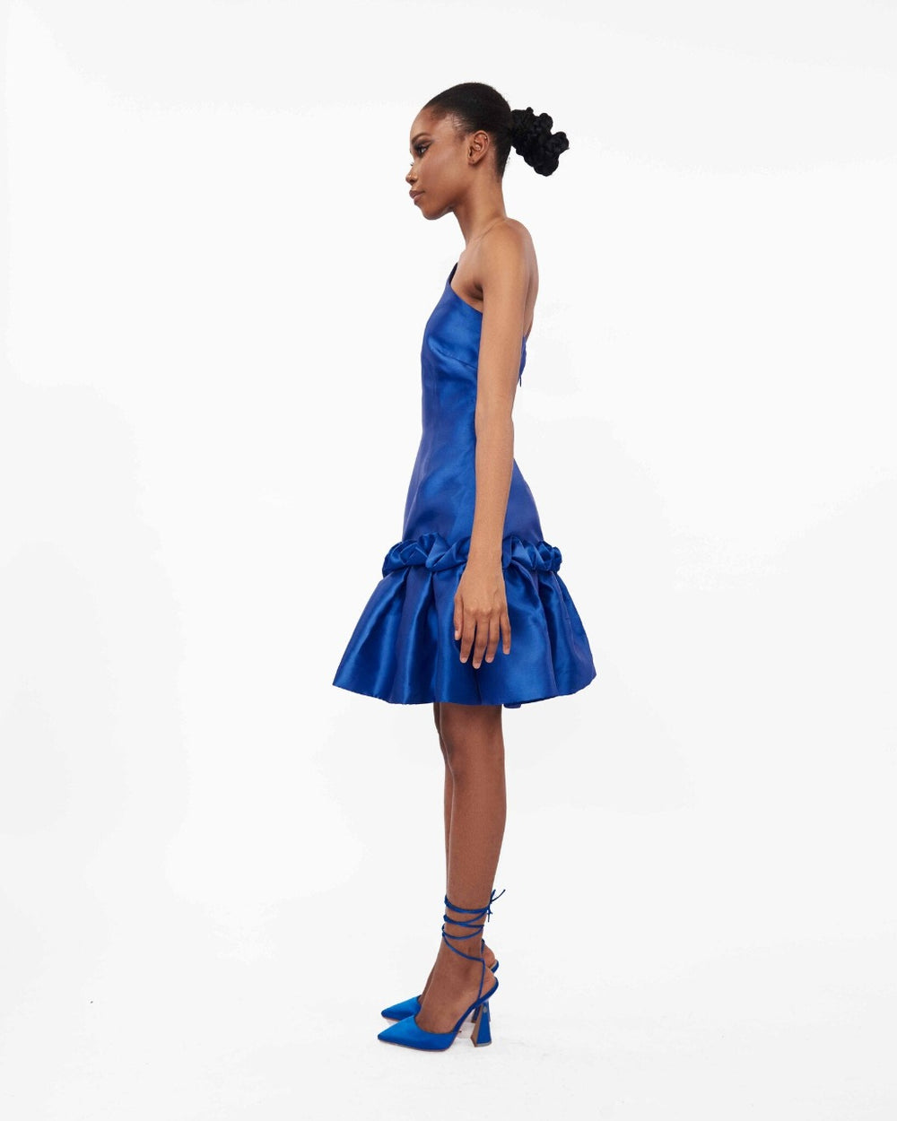 The side of a model wearing a one-shoulder blue dress with drop waist ruffle detailing 