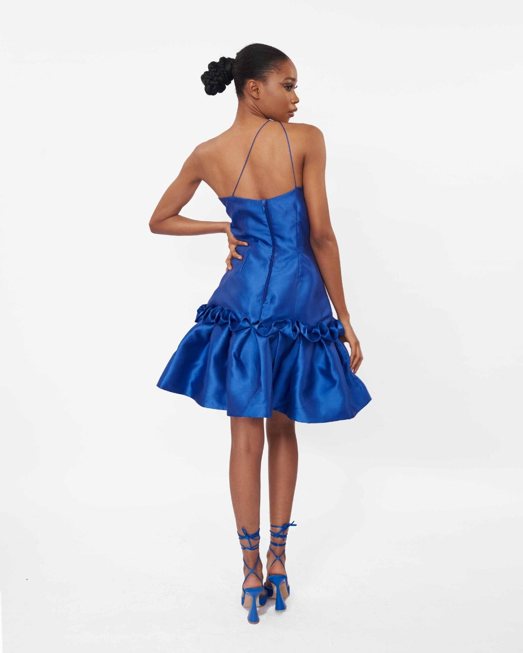 The back of a model wearing a one-shoulder blue dress with drop waist ruffle detailing