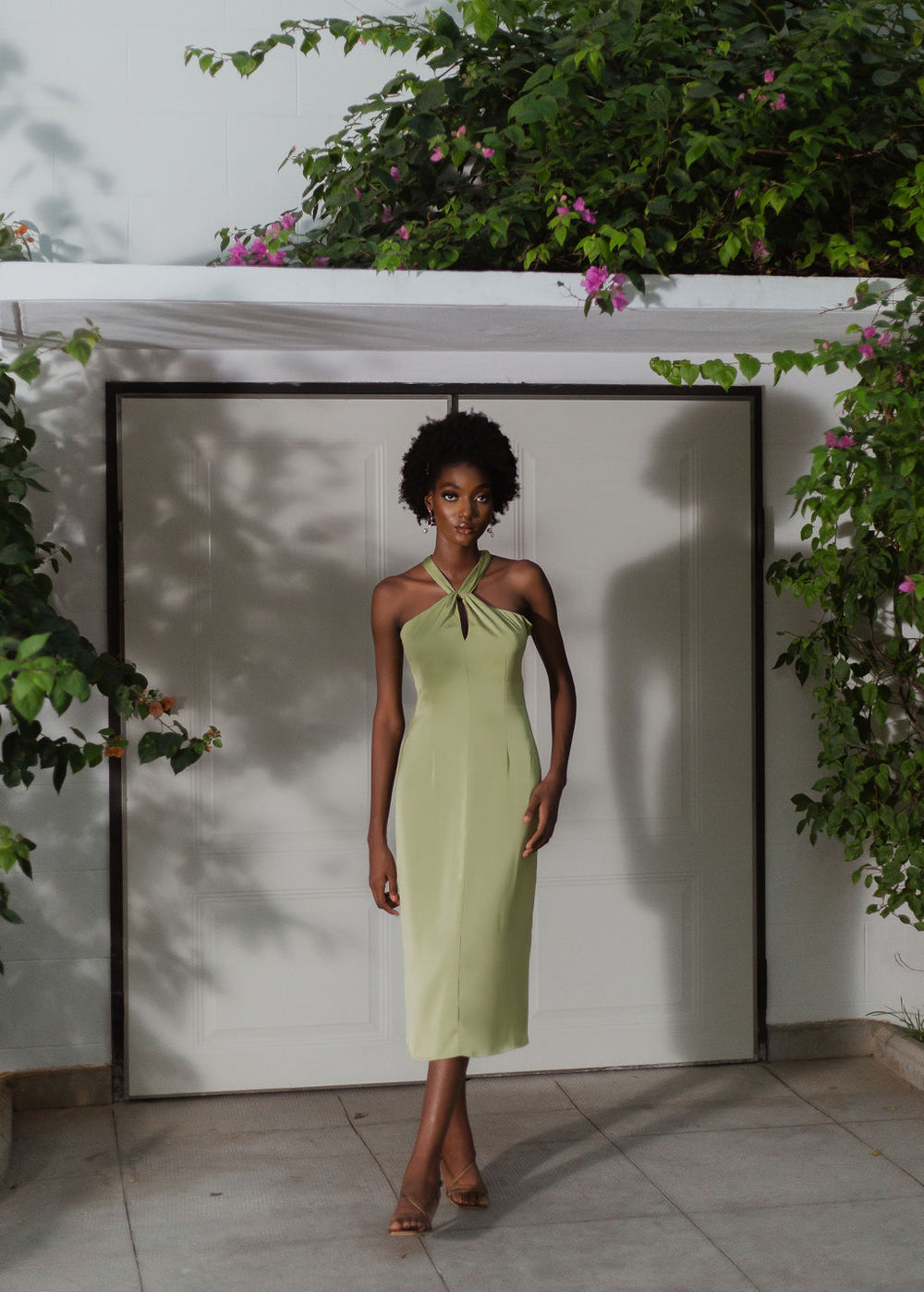 A model wearing an olive halter neck dress in front of a house