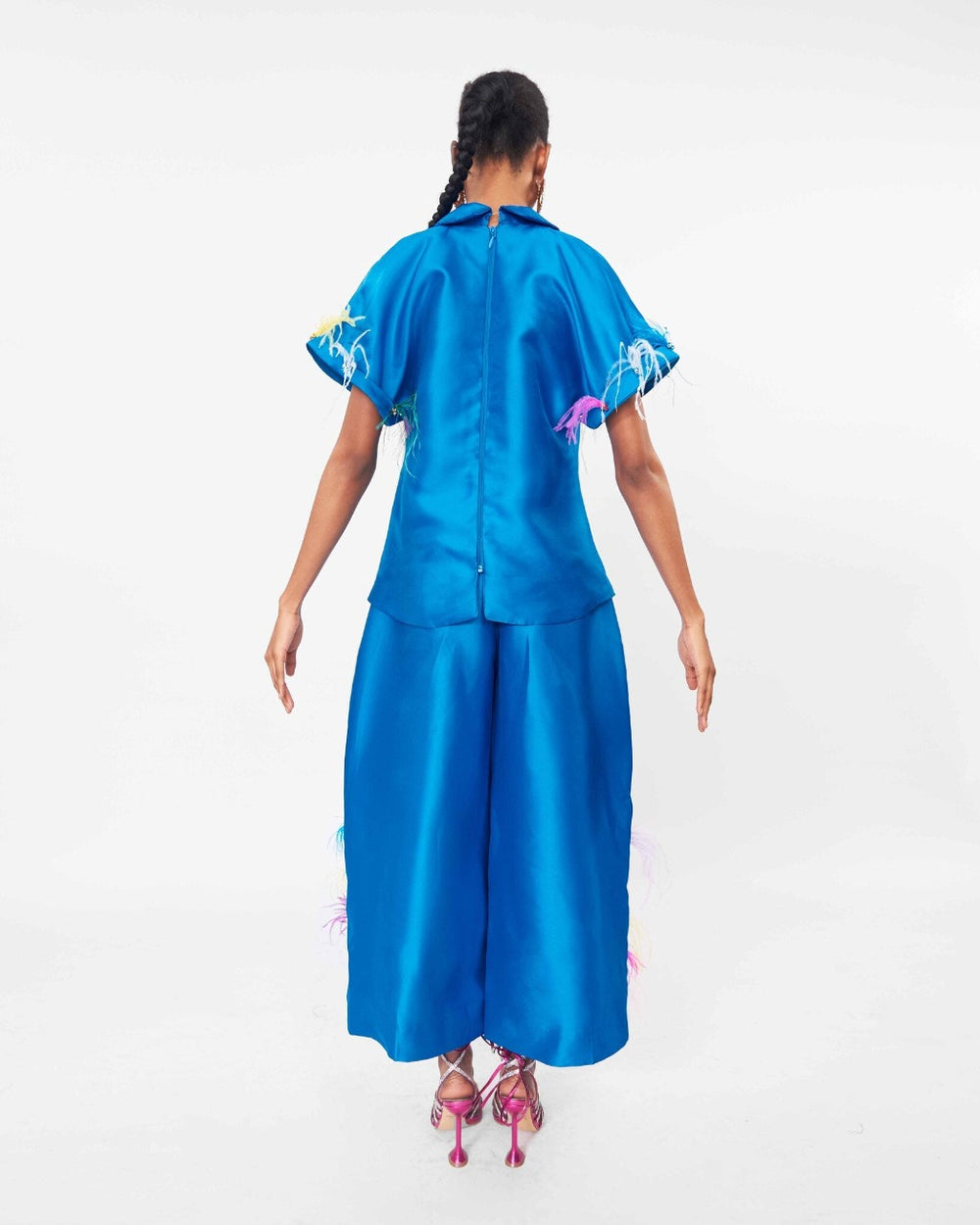 The back of a model wearing a Turquoise top with criss-cross neckline and Turquoise pants with a waist pleat detail and ostrich feathers embellishments
