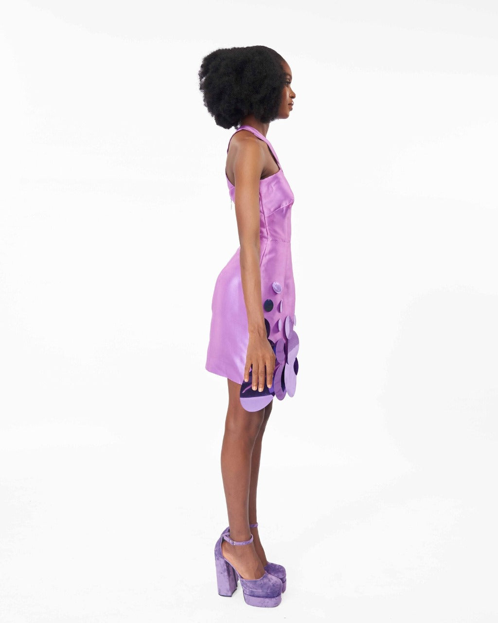 The side of a model wearing a Lilac mini dress with a criss-cross neckline and sequins embellishment at the hem