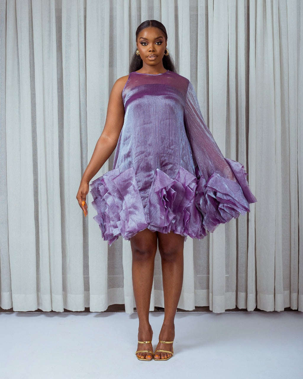 A model wearing a Purple asymetric sleeve mini dress with ruffles and silk slip lining in front of white curtains