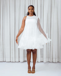 A model wearing a White asymetric sleeve mini dress with ruffles and silk slip lining in front of white curtains