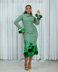 A model wearing a Green top with cut-out neckline detail and sequins embellishment at the neckline and sleeve hem and a Green high waist midi skirt with sequins embellishment in front of white curtains