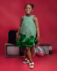 A kid model wearing a Green dress with sequins embellishment in a red room