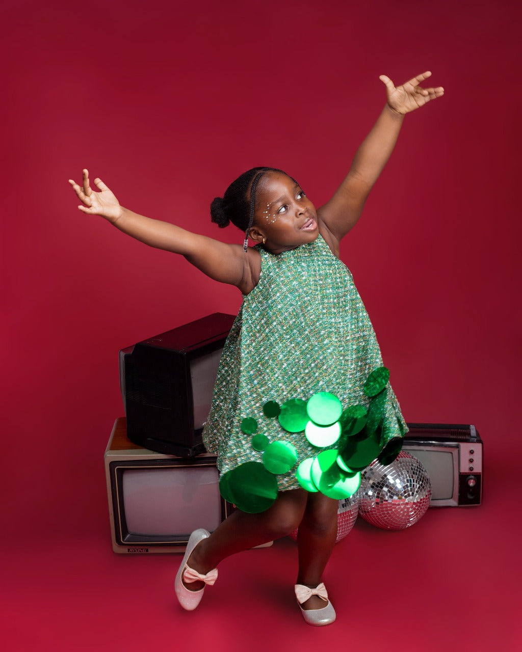 A kid model wearing a Green dress with sequins embellishment in a red room
