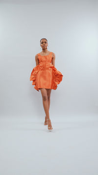A model posing while wearing an Orange crop top and an Orange mini skirt with ruffles on it