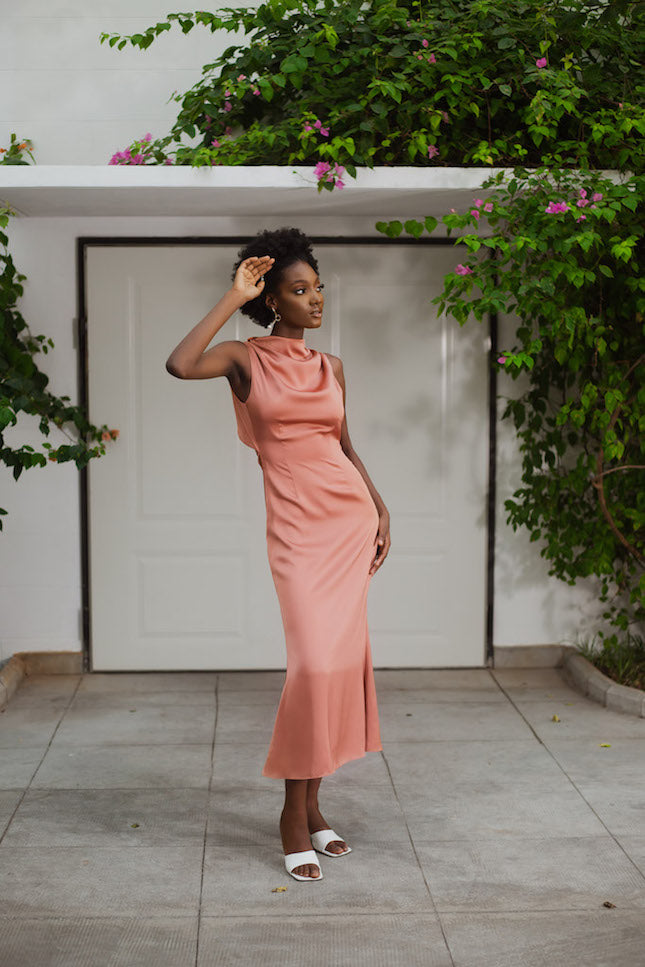 a model posing in front of a house while wearing a rose gold dress