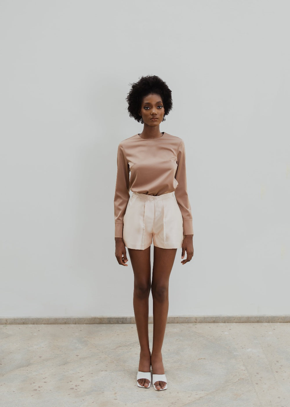 A model wearing a brown top and Nude colored shorts