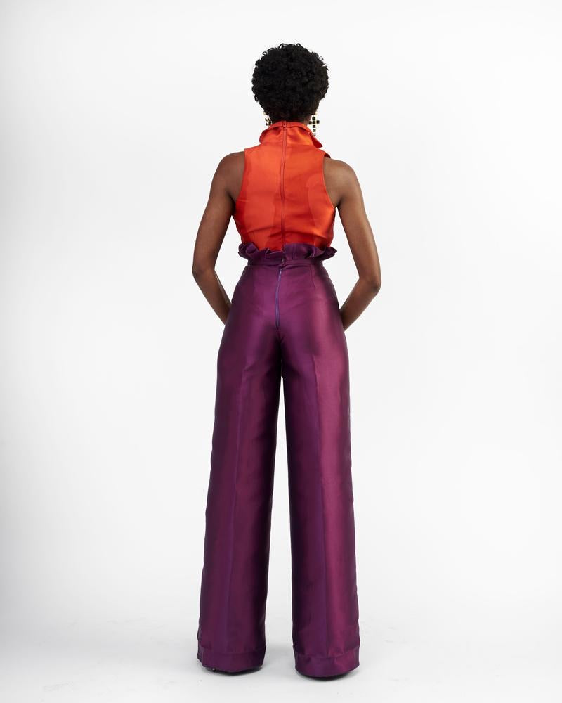 The back of A model wearing purple silk satin pants with an orange top 